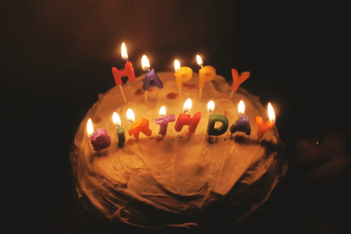 Tarta de chocolate con velas encendidas en forma de letras que dicen «Happy Birthday», en penumbra
