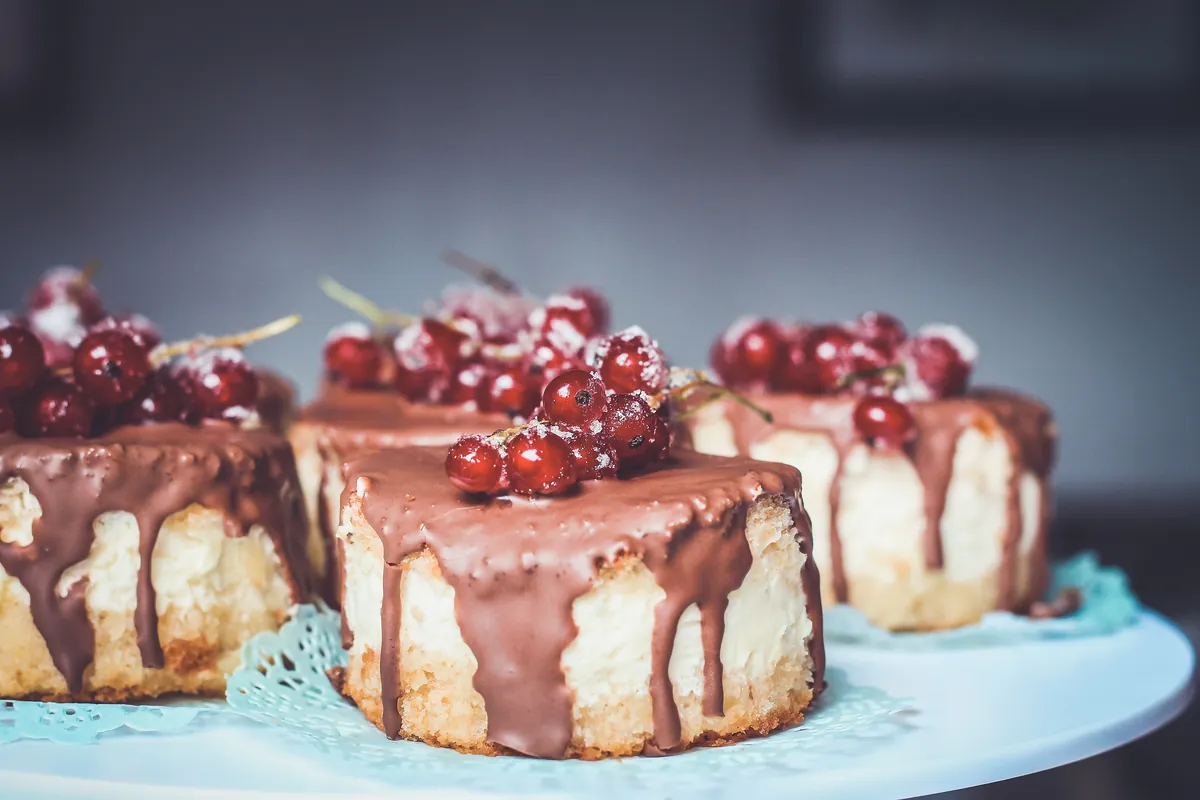 Tres tartas pequeñas bañadas en chocolate, con grosellas rojas por encima